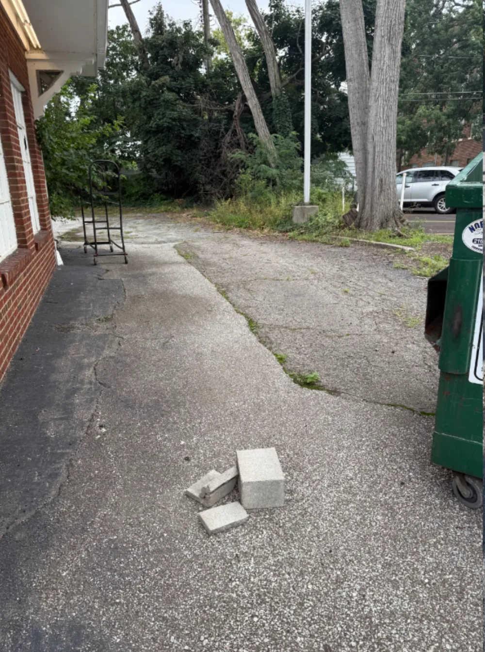 Before: rear yard and dumpster area at a Mr. Tire shop in Lakewood, OH, weathered asphalt with grass growing through the cracks