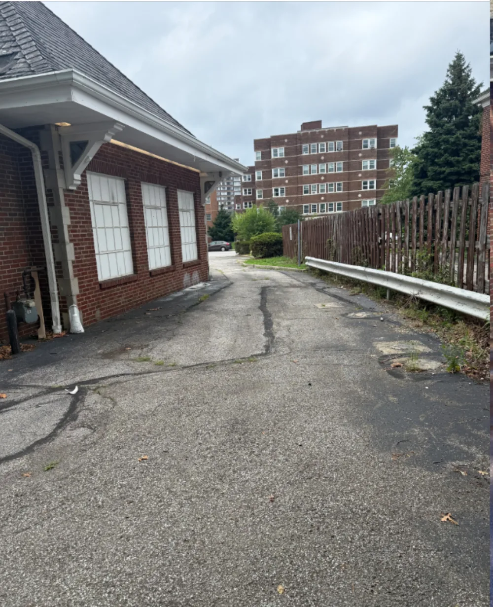 Before: side service drive at a Mr. Tire shop in Lakewood, OH, gray cracked asphalt with weeds along the guardrail