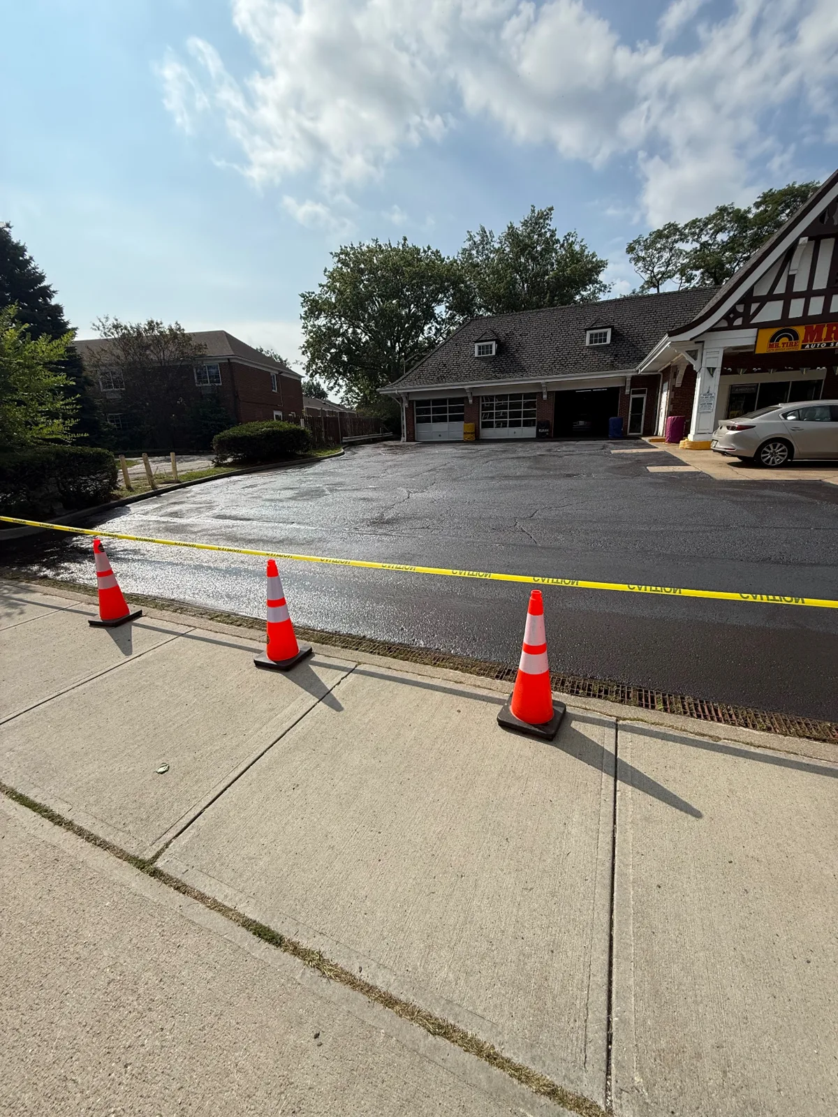Freshly sealcoated Mr. Tire customer parking lot taped off with cones in Lakewood